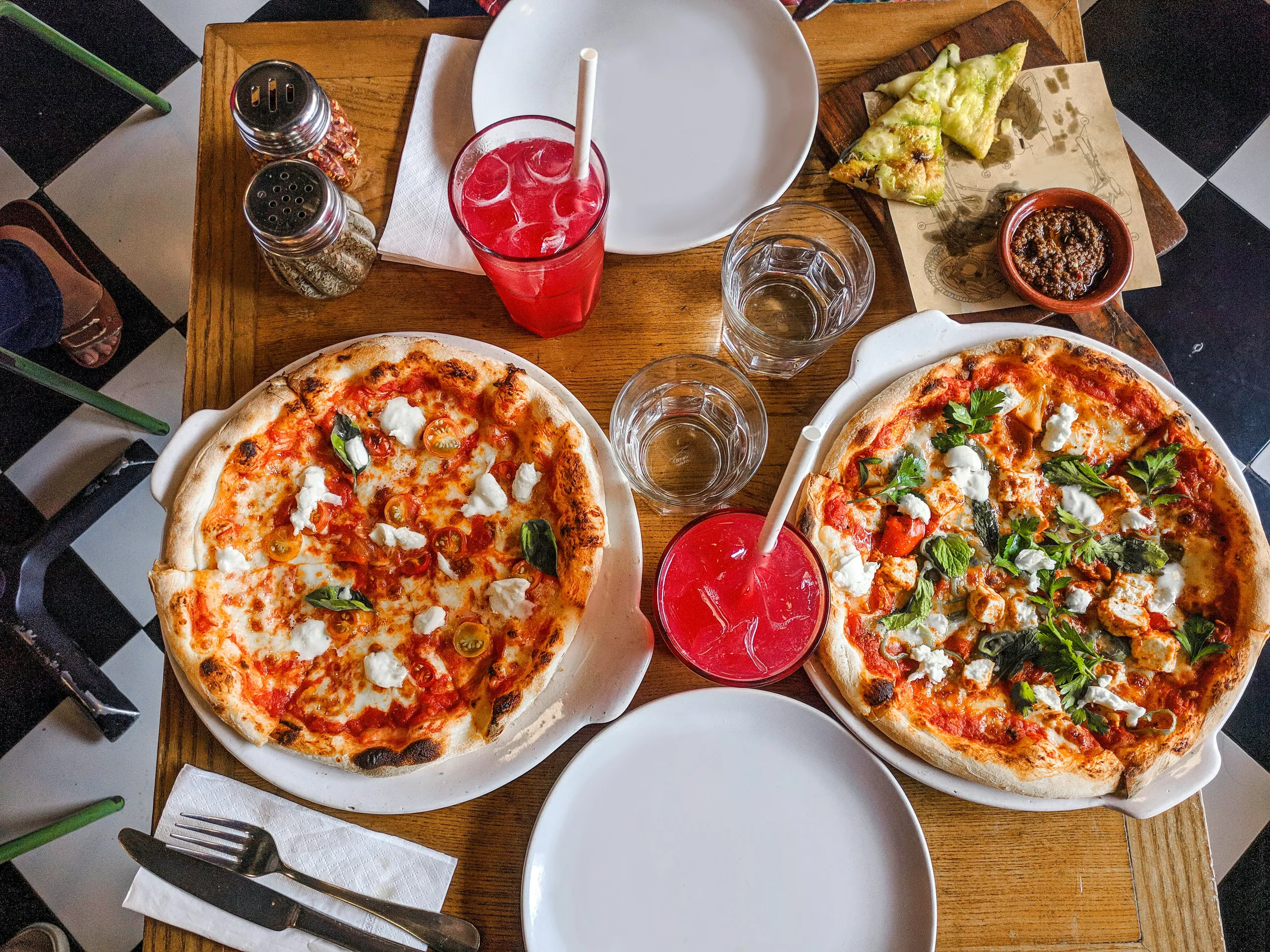 Dos pizzas sobre mesa de madera con bebidas